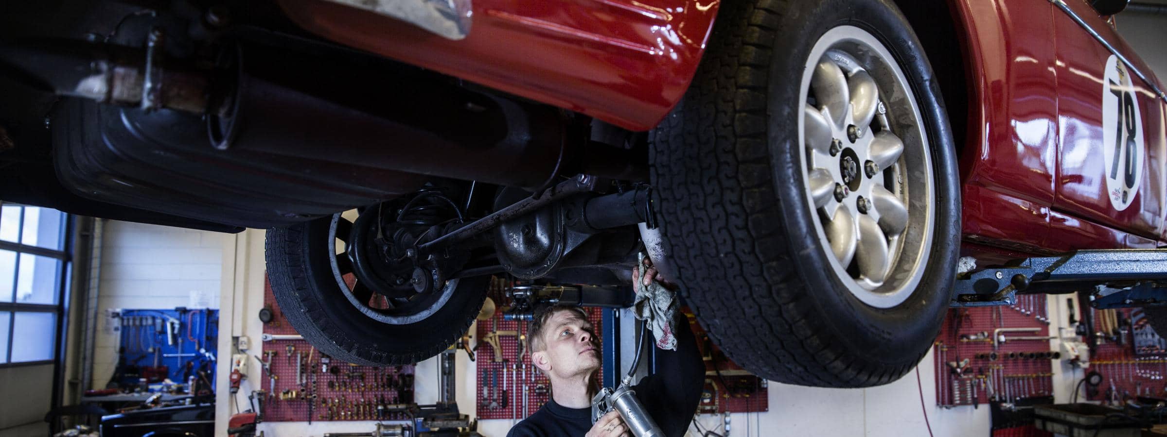 Mekaniker arbejder under en løftet rød bil på et autoværksted