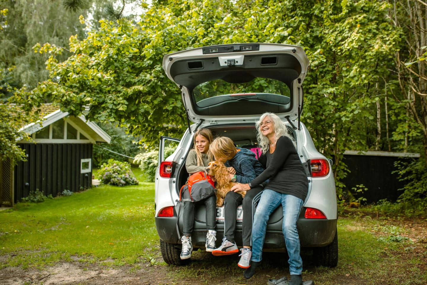 Familie som sidder i bilens åbne bagagerum - de er på sikker bilferie