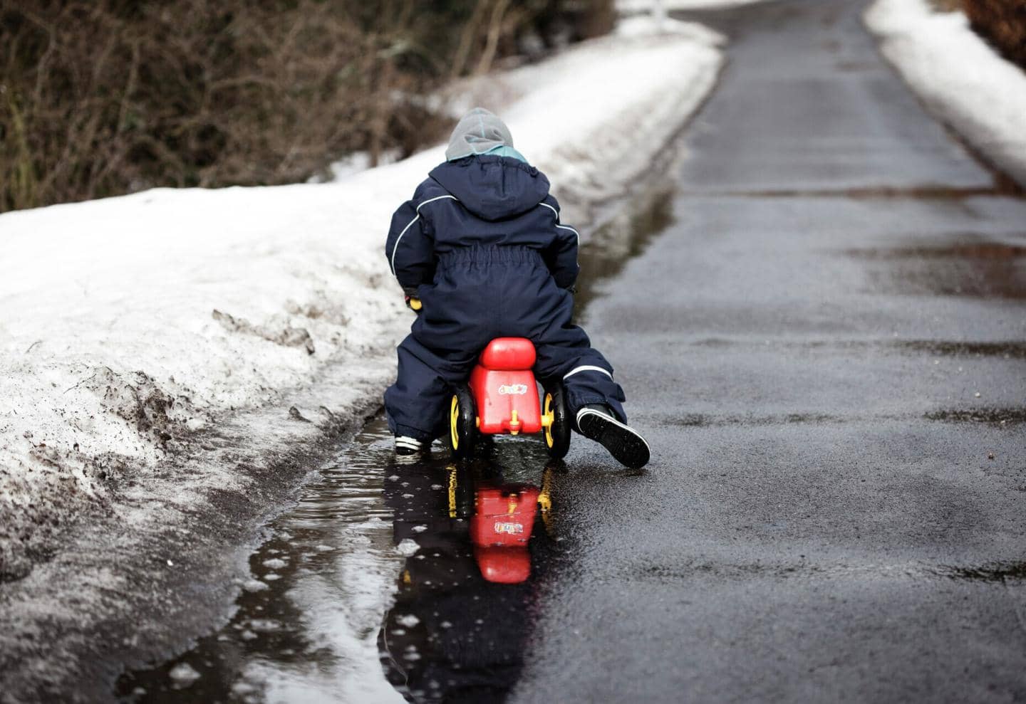 Barn i flyverdragt på legescooter på vej med sne i kanten